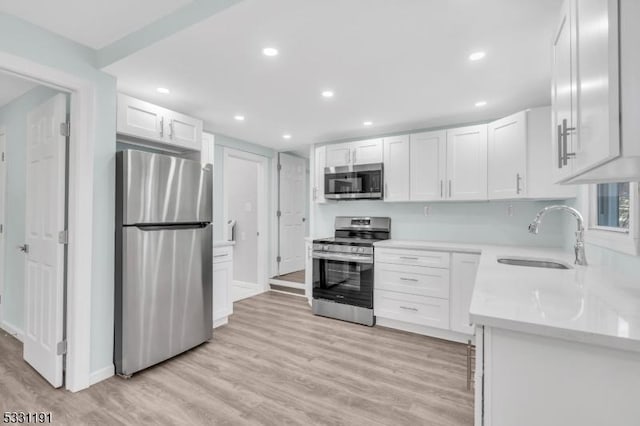 kitchen with appliances with stainless steel finishes, light hardwood / wood-style flooring, white cabinets, and sink