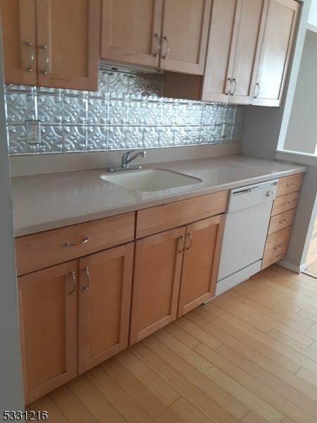 kitchen featuring backsplash, sink, white dishwasher, and light wood-type flooring