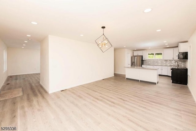 kitchen with white cabinetry, stainless steel fridge, decorative light fixtures, decorative backsplash, and a kitchen island