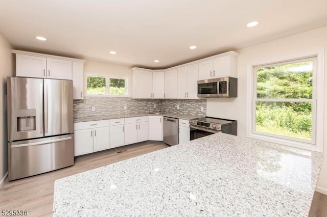 kitchen with a healthy amount of sunlight, light stone countertops, white cabinetry, and stainless steel appliances