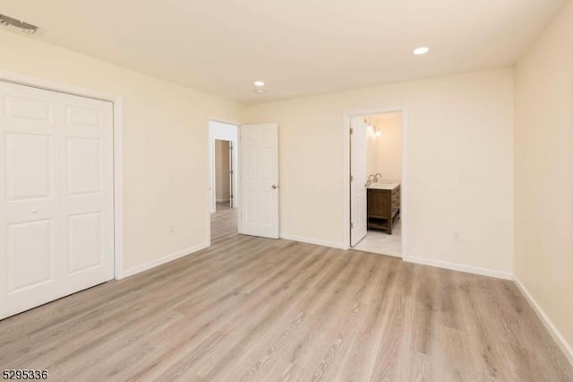 unfurnished bedroom with light hardwood / wood-style floors, ensuite bath, and a closet