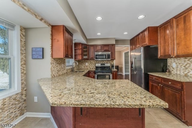 kitchen featuring kitchen peninsula, decorative backsplash, a kitchen breakfast bar, stainless steel appliances, and sink