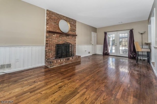 unfurnished living room featuring french doors, a brick fireplace, and dark wood-type flooring