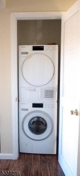 clothes washing area with stacked washing maching and dryer and dark hardwood / wood-style floors