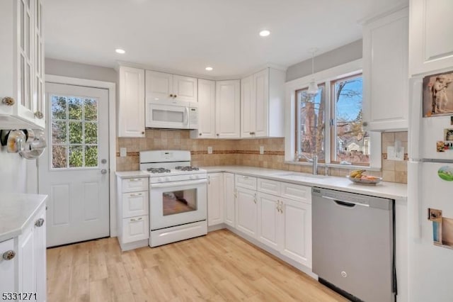 kitchen with white appliances, light countertops, a sink, and white cabinetry