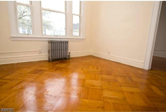 unfurnished room featuring a wealth of natural light, radiator heating unit, and parquet flooring