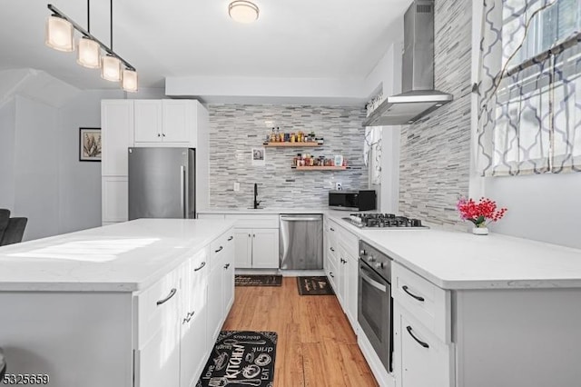 kitchen featuring white cabinetry, wall chimney exhaust hood, stainless steel appliances, decorative light fixtures, and decorative backsplash