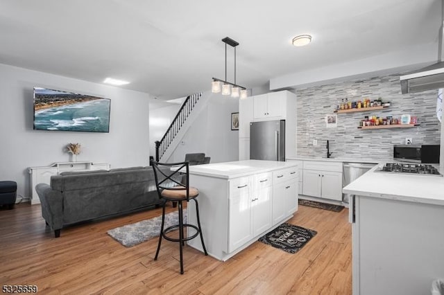 kitchen with tasteful backsplash, stainless steel appliances, decorative light fixtures, white cabinetry, and a kitchen island