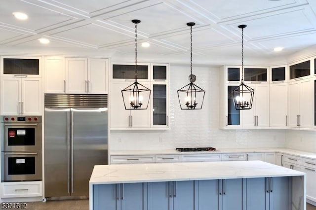 kitchen with appliances with stainless steel finishes, hanging light fixtures, light stone countertops, a kitchen island, and white cabinetry