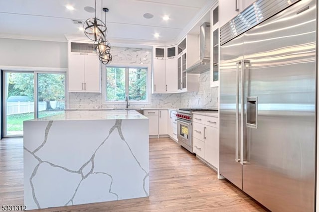 kitchen featuring light stone countertops, white cabinets, wall chimney range hood, premium appliances, and pendant lighting