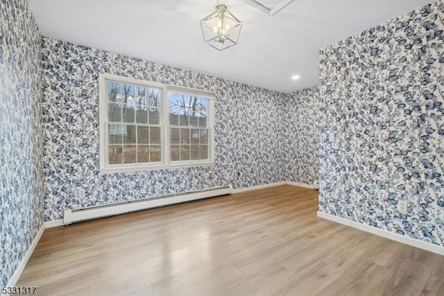 spare room with baseboard heating, a chandelier, and wood-type flooring