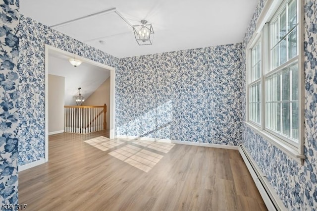 unfurnished room featuring baseboard heating, a wealth of natural light, hardwood / wood-style floors, and a notable chandelier