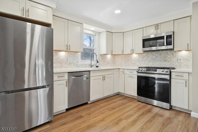 kitchen with light hardwood / wood-style floors, appliances with stainless steel finishes, ornamental molding, white cabinets, and sink