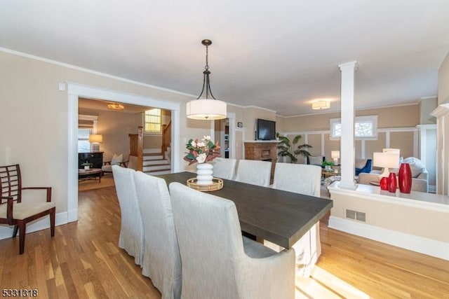 dining area with decorative columns, ornamental molding, and light wood-type flooring