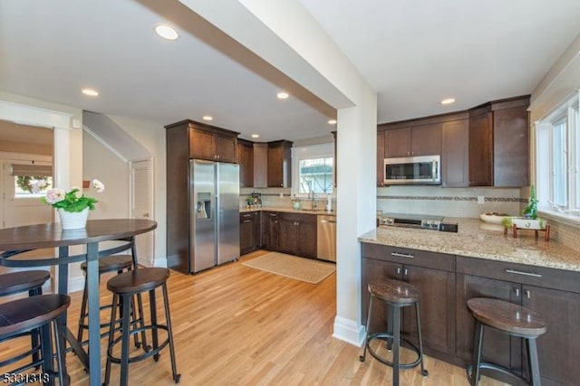 kitchen featuring appliances with stainless steel finishes, tasteful backsplash, light stone counters, and dark brown cabinets