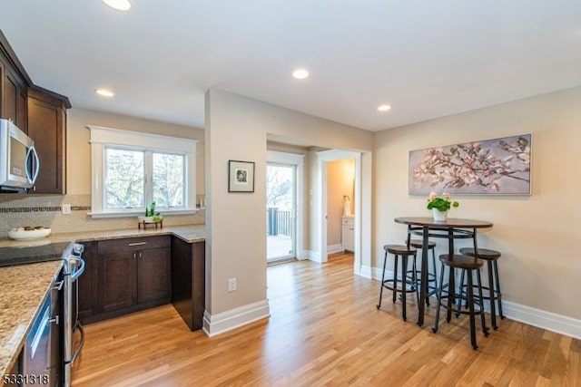 kitchen featuring backsplash, light stone counters, light hardwood / wood-style flooring, and stainless steel appliances