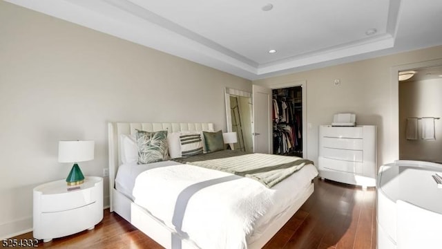 bedroom featuring a tray ceiling, a spacious closet, a closet, and dark wood-type flooring