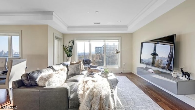 living room with a raised ceiling, dark hardwood / wood-style flooring, and ornamental molding