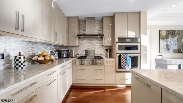 kitchen featuring appliances with stainless steel finishes, tasteful backsplash, wall chimney range hood, cream cabinets, and dark hardwood / wood-style floors