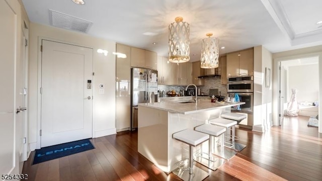 kitchen with dark hardwood / wood-style floors, stainless steel appliances, hanging light fixtures, and an island with sink