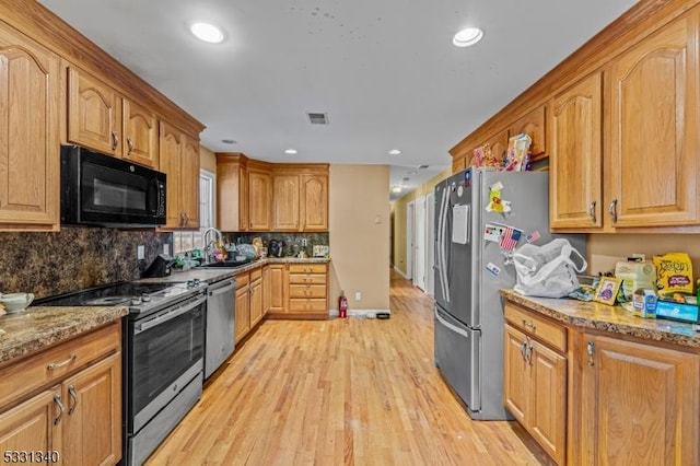 kitchen featuring light stone countertops, appliances with stainless steel finishes, backsplash, sink, and light hardwood / wood-style flooring