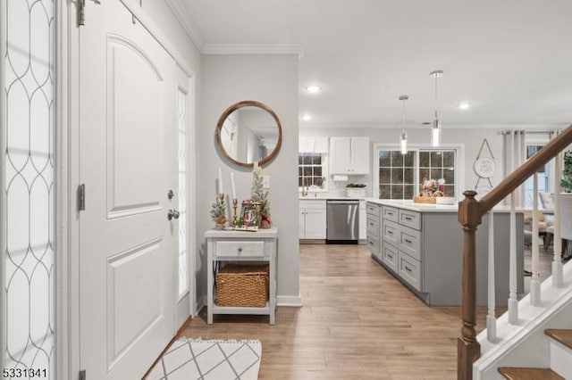 interior space featuring dishwasher, white cabinets, light hardwood / wood-style flooring, ornamental molding, and decorative light fixtures