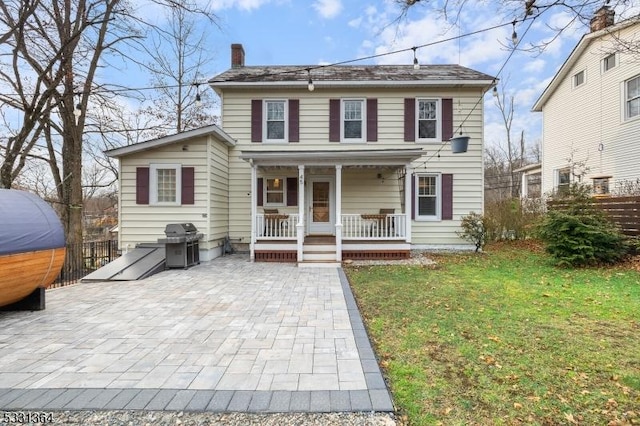 colonial inspired home featuring covered porch, a patio, and a front lawn