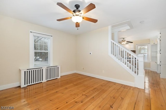 empty room featuring plenty of natural light, ceiling fan, light wood-type flooring, and radiator