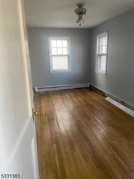 spare room with dark wood-type flooring, a healthy amount of sunlight, and a baseboard heating unit