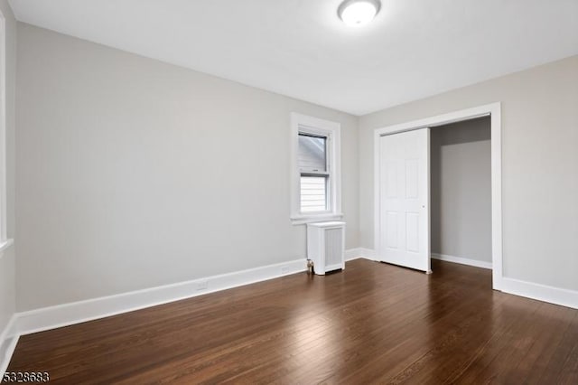 unfurnished bedroom featuring a closet, dark hardwood / wood-style floors, and radiator