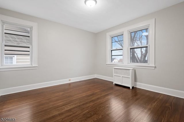 empty room with dark hardwood / wood-style flooring and radiator heating unit