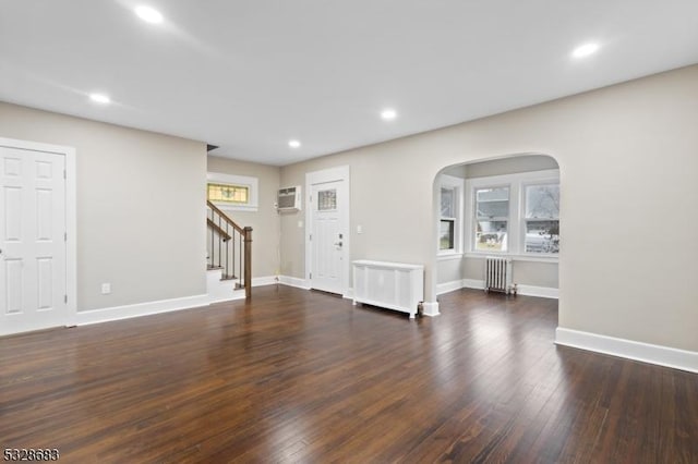 unfurnished living room with radiator heating unit, a wall unit AC, and dark wood-type flooring