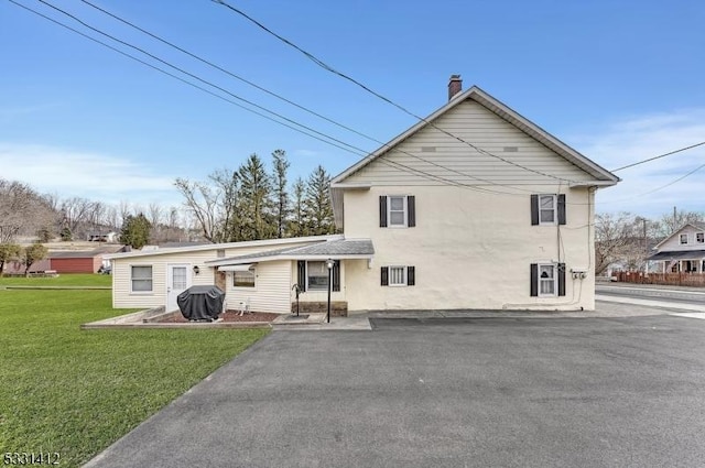 rear view of house featuring a lawn, a chimney, and stucco siding