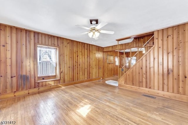 unfurnished living room featuring wooden walls, visible vents, stairway, hardwood / wood-style flooring, and a ceiling fan