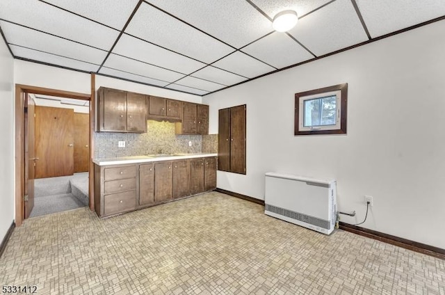 kitchen featuring heating unit, a sink, decorative backsplash, light countertops, and a paneled ceiling