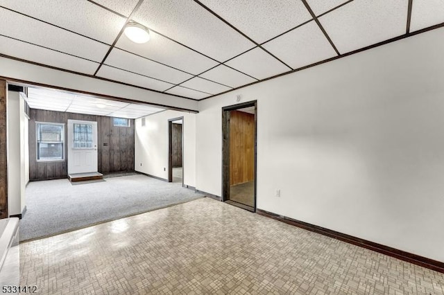 spare room with wooden walls, a paneled ceiling, and baseboards