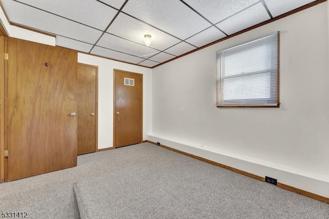 carpeted empty room with baseboards, visible vents, and a drop ceiling