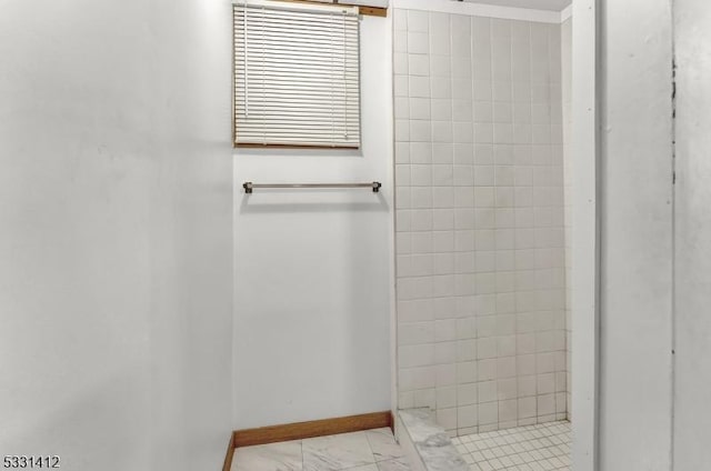 bathroom featuring a tile shower, marble finish floor, and baseboards