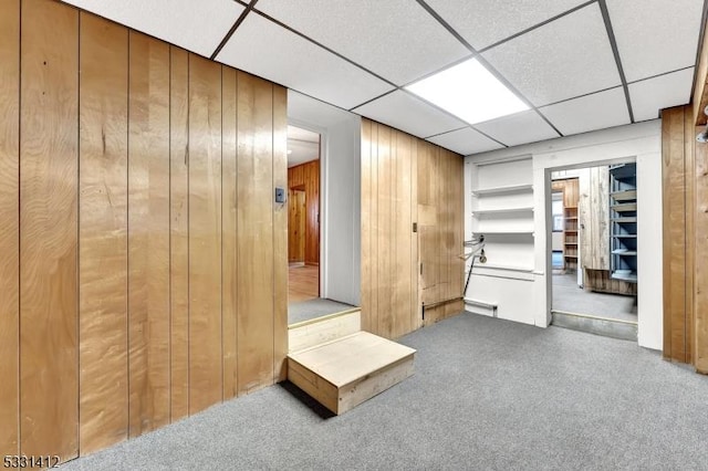 empty room featuring wood walls, a paneled ceiling, and carpet