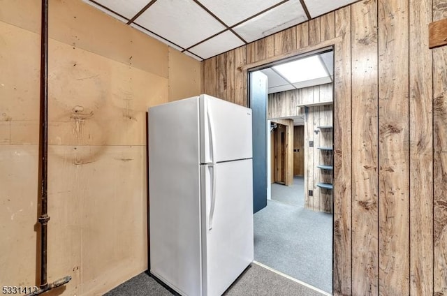 kitchen with carpet flooring, a paneled ceiling, wood walls, and freestanding refrigerator