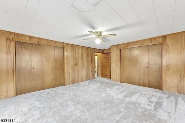 unfurnished bedroom with wooden walls, a ceiling fan, and carpet