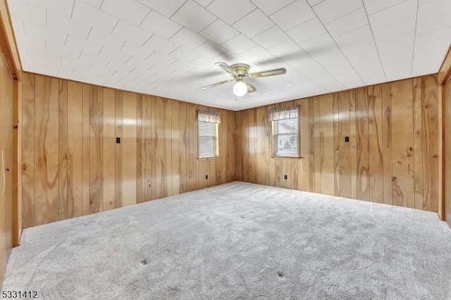 carpeted empty room with wood walls and a ceiling fan