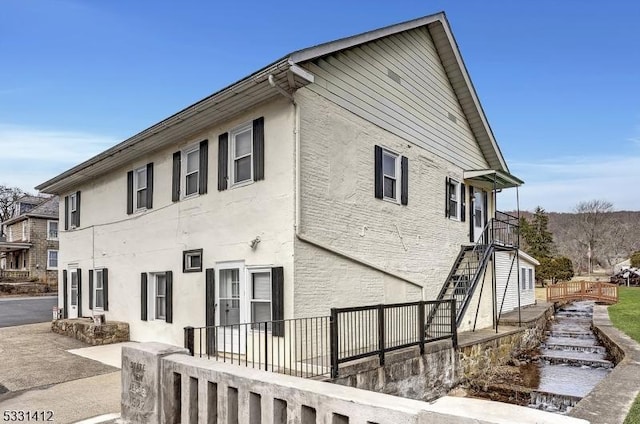 view of side of home with stairway, fence, and stucco siding