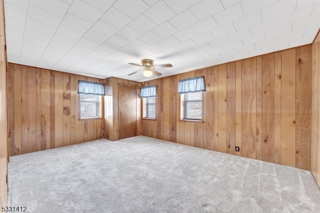 carpeted spare room featuring wood walls and a ceiling fan