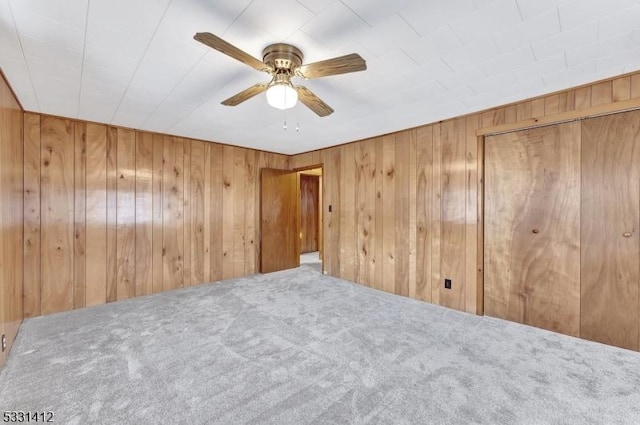 unfurnished bedroom with wooden walls, carpet, and ceiling fan