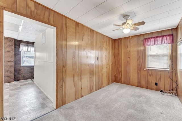 carpeted spare room with a ceiling fan, wooden walls, a healthy amount of sunlight, and brick wall