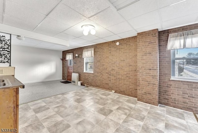 unfurnished room with a drop ceiling and brick wall