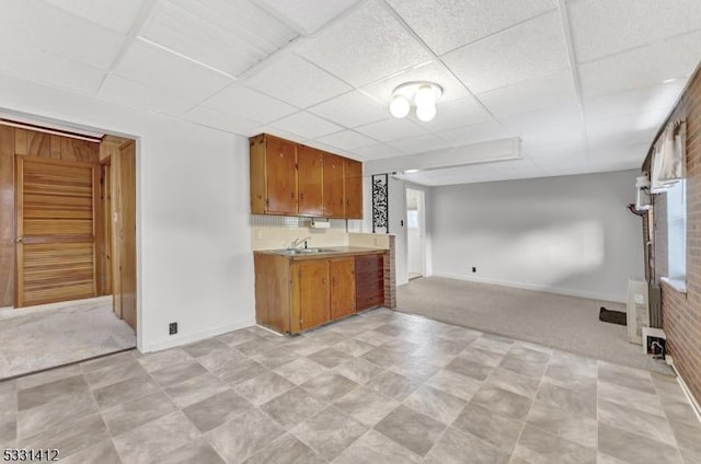 kitchen with a drop ceiling, brown cabinets, light colored carpet, and open floor plan