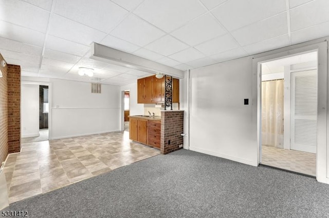 unfurnished living room featuring light colored carpet, a paneled ceiling, and baseboards