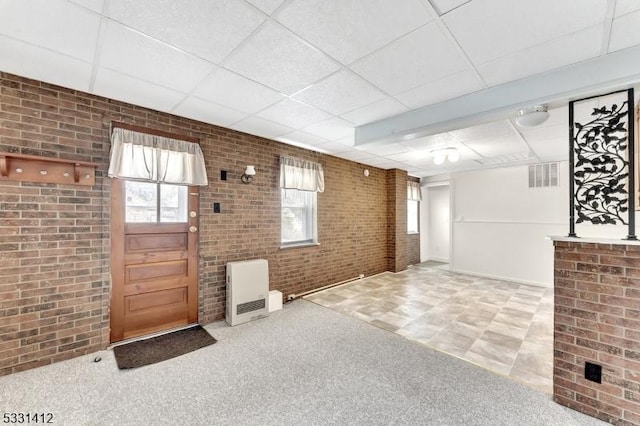 interior space featuring heating unit, visible vents, brick wall, and a paneled ceiling